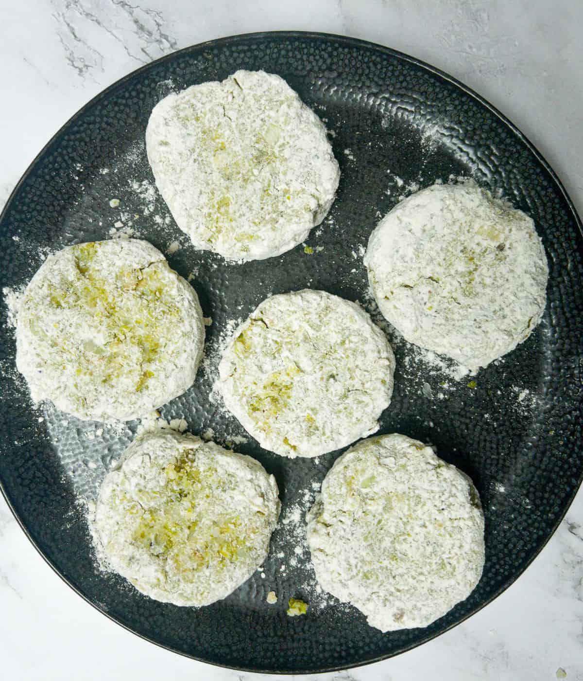 Bubble & squeak patties uncooked, coated in flour on a plate.