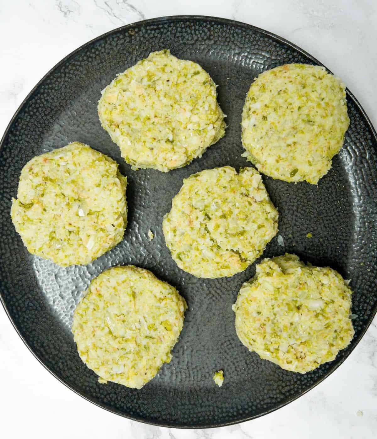 6 uncooked bubble and squeak cakes on a black plate.