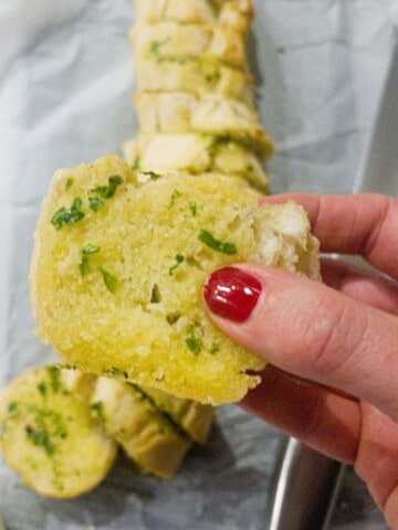 Someone holding a piece of garlic bread with the rest of the loaf behind.