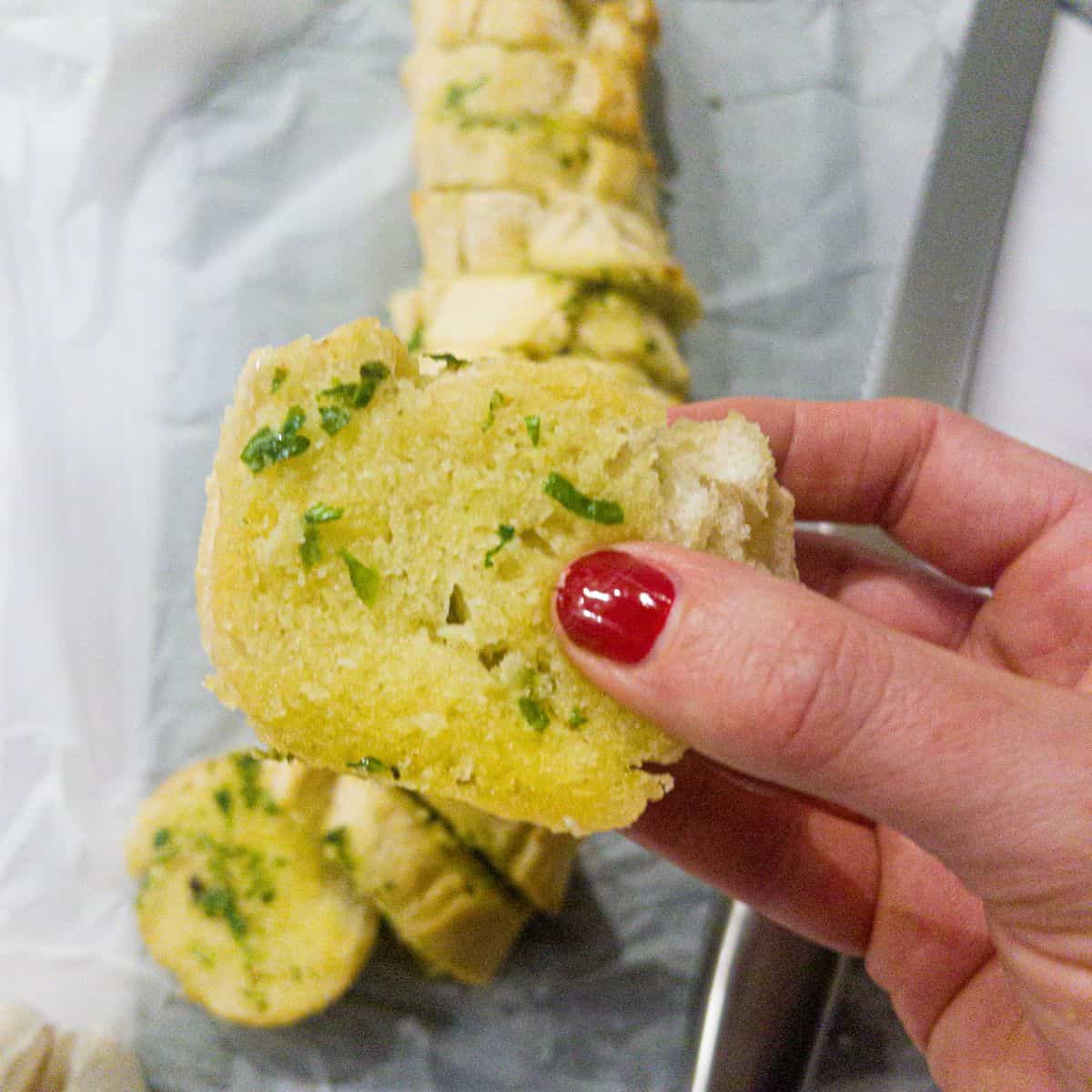 Someone holding a piece of garlic bread with the rest of the loaf behind.