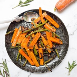 roasted carrots and green beans on a black plate witha rosemary and carrot garnish.