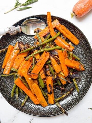 roasted carrots and green beans on a black plate witha rosemary and carrot garnish.