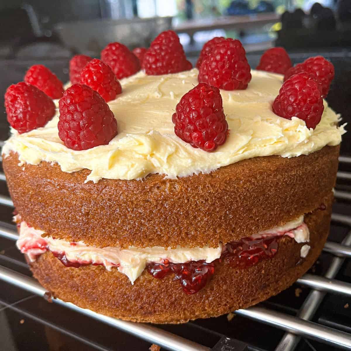Victoria sponge with cream and jam in the middle, topped with buttercream and raspberries.