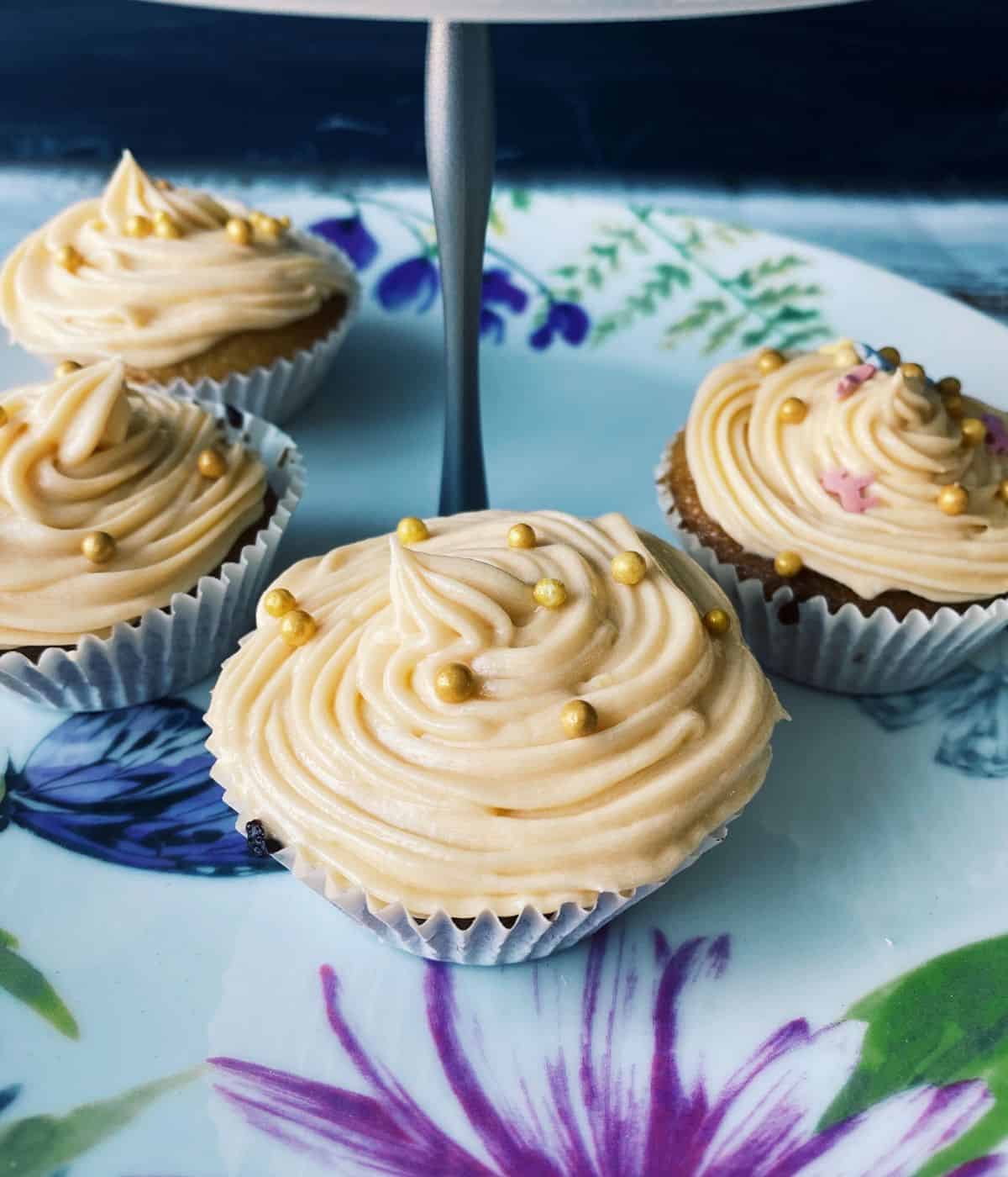 Close up shot of cupcakes with vanilla frosting and gold sugar balls.