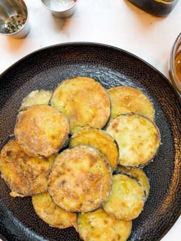 Fried aubergine rounds on a plate with a bowl of honey next to it.