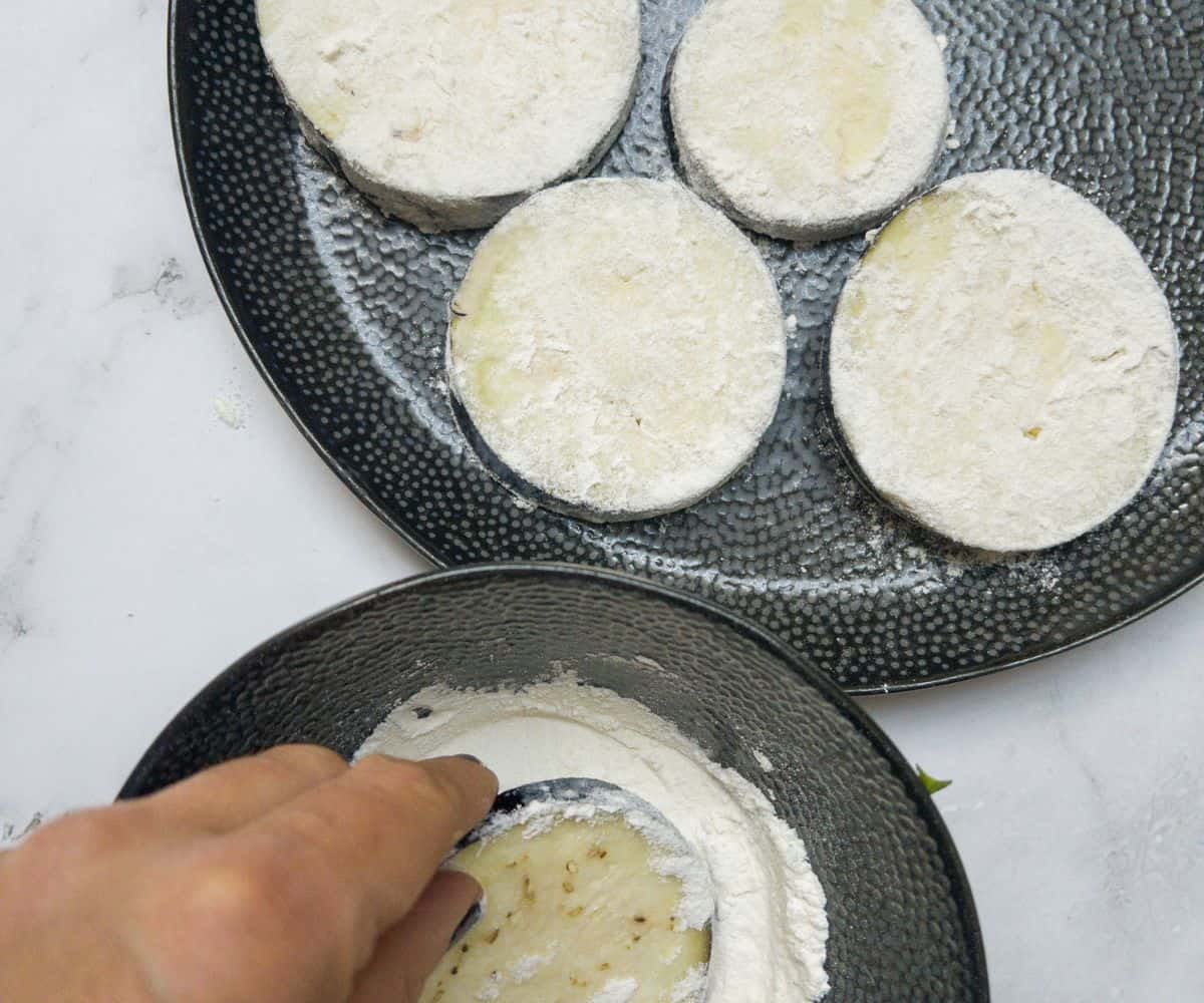 Aubergine rounds being coated in flour and placed on a plate.