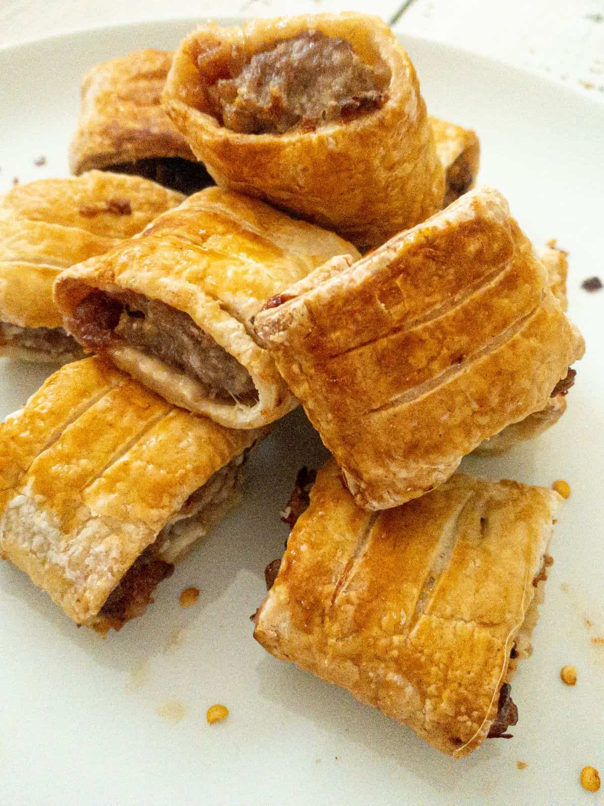 mini gluten free sausage rolls piled on top of each other on a white plate.