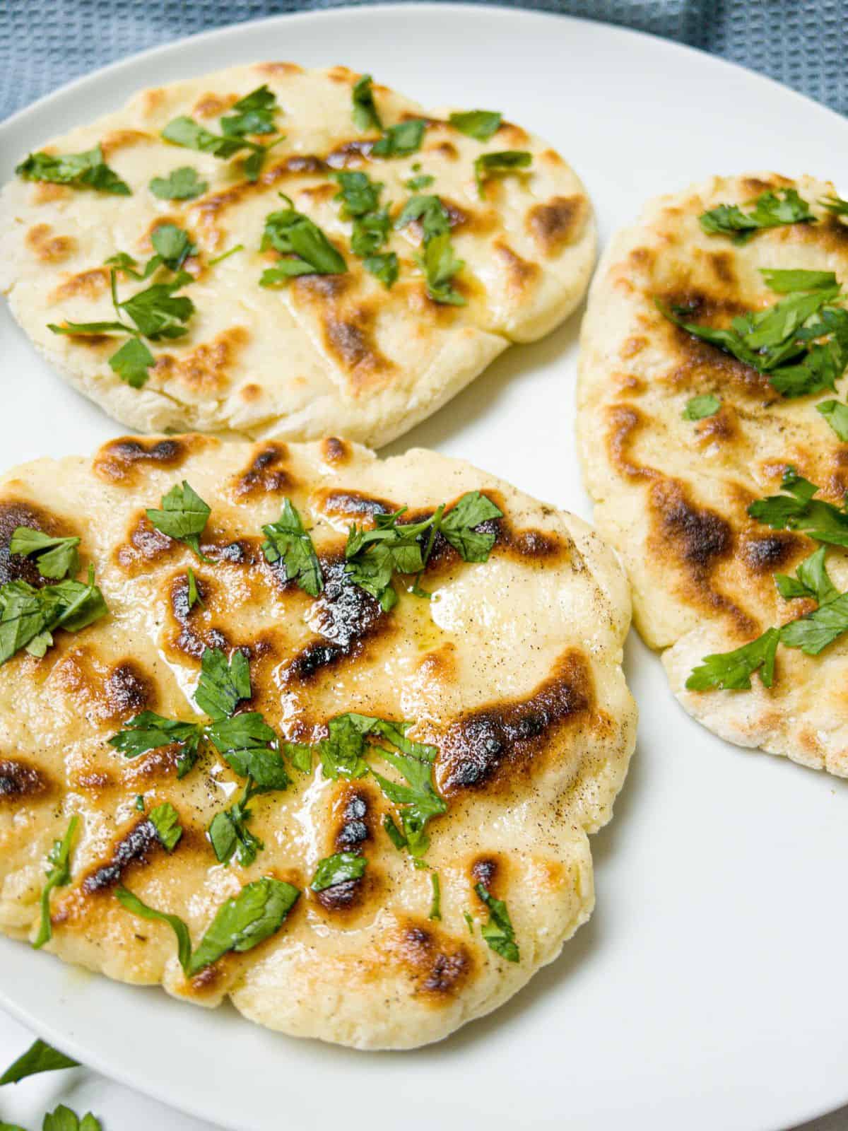 close up shot of three naan breads garnished with parsley on a white plate.