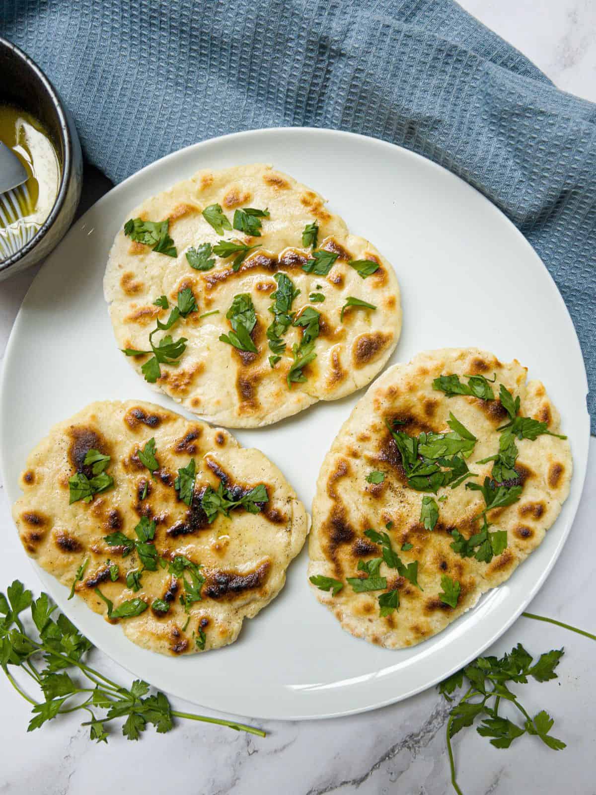 3 naan breads on a white plate garnished with parsley.