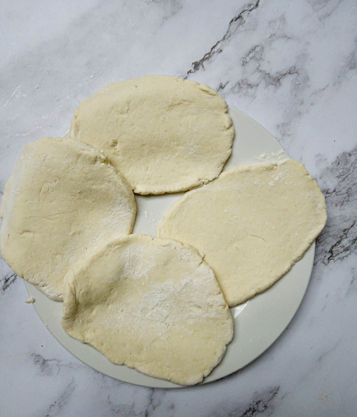 Uncooked homemade gluten free naan breads on a white plate.