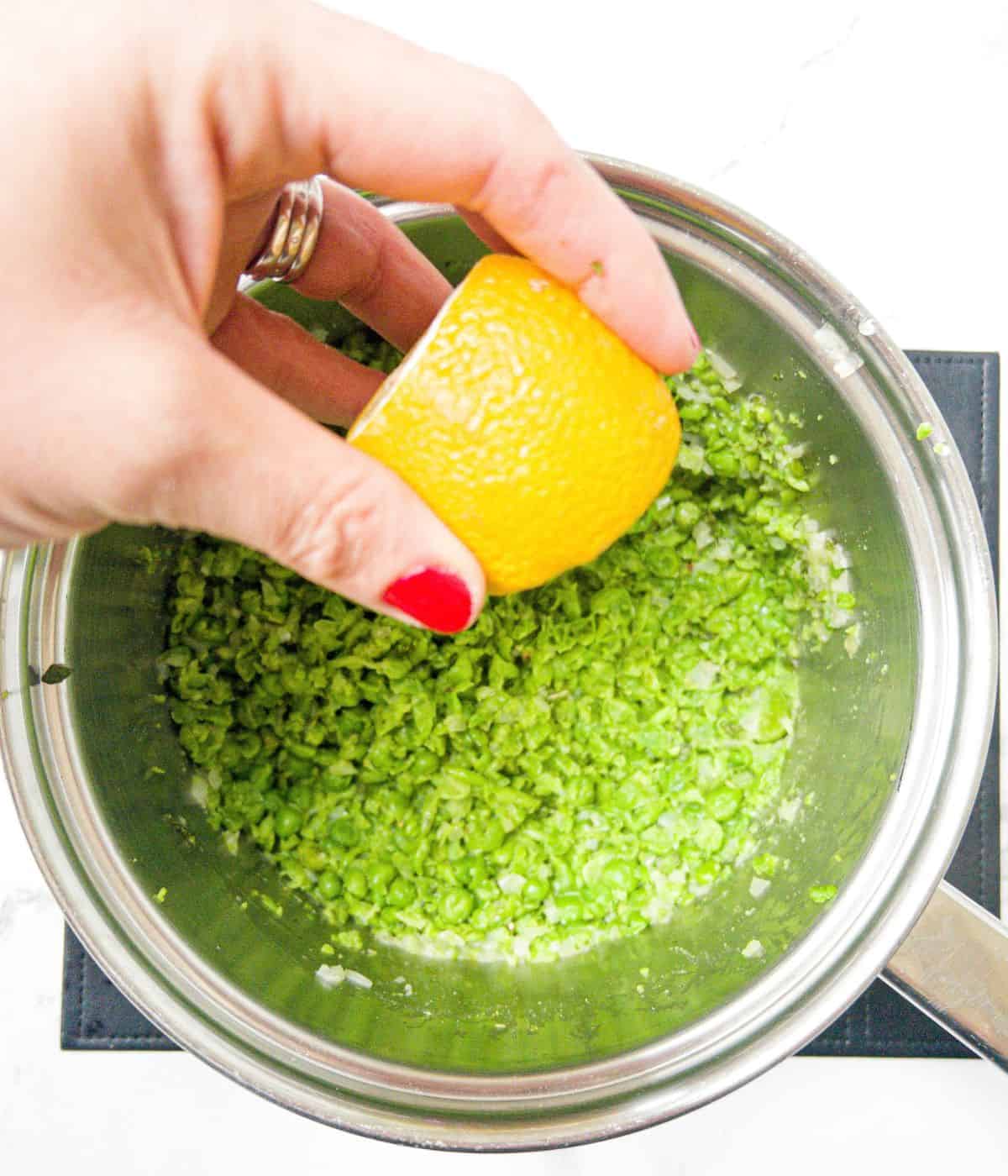 Lemon being squeezed into a pan of mushy peas.