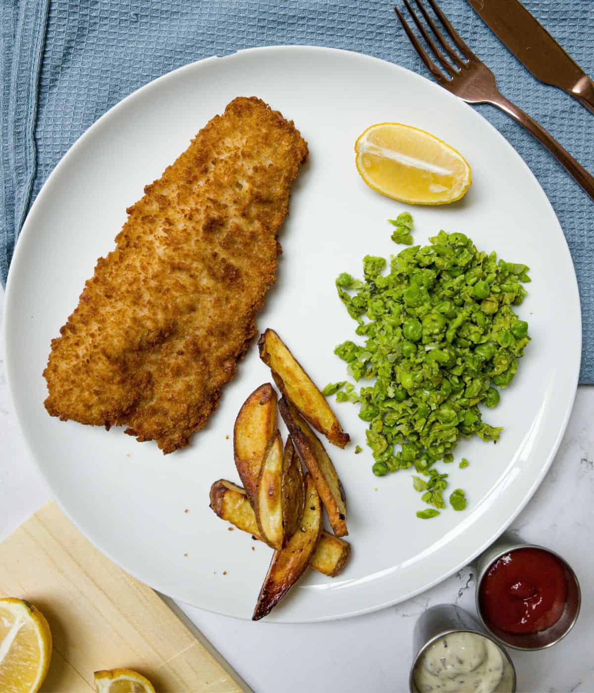 Fish, chips, mushy peas and lemon on a plate.