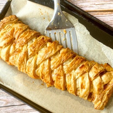 Sausage plait on a baking tray with a spatula.