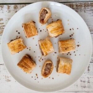 mini sausage rolls on a white plate with a chilli garnish.