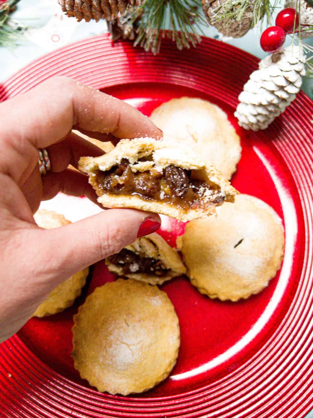 mince pies on a plate with one cut in half & being held so you can see the mincemeat inside.
