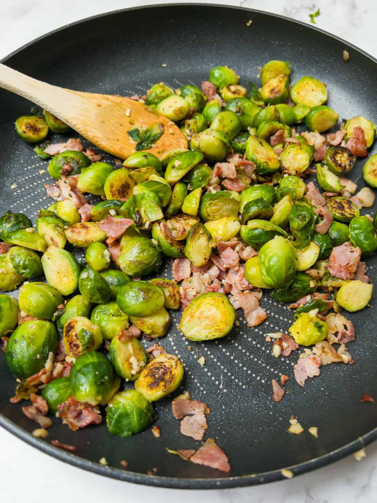 Brussel sprouts with garlic and bacon frying in a pan.
