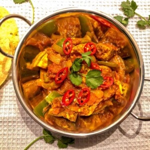 Chicken curry in a silver curry bowl, garnished with fresh red chilli and coriander.