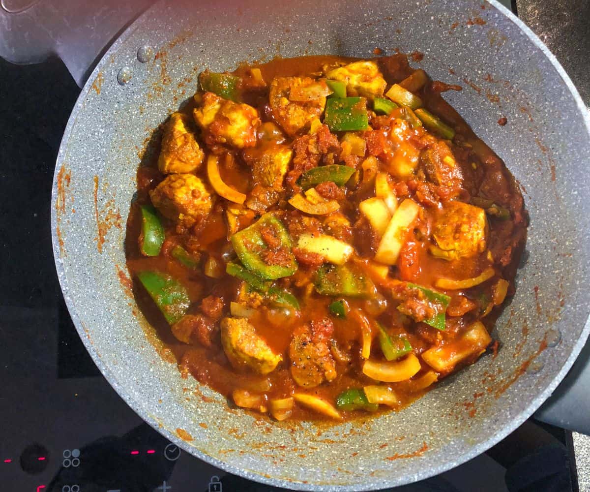 Chicken curry with peppers cooking in a frying pan.