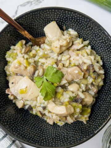 A bowl of chicken and leek risotto with a spoon in the bowl.