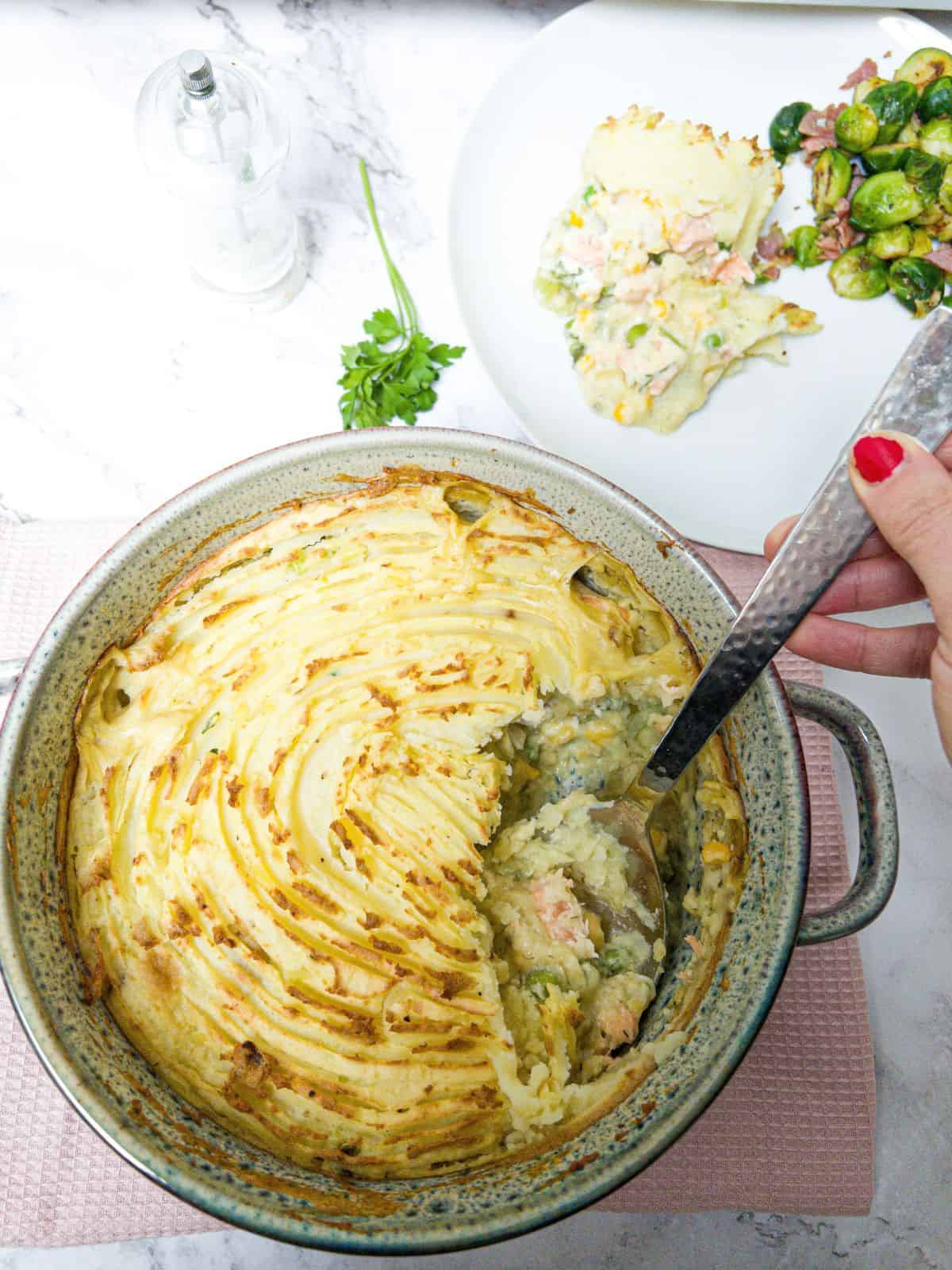 Dairy free fish pie in a casserole dish with a hand spooning out a portion.