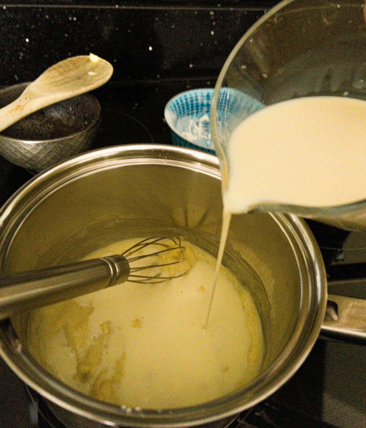 milk being poured into a white sauce in a saucepan.