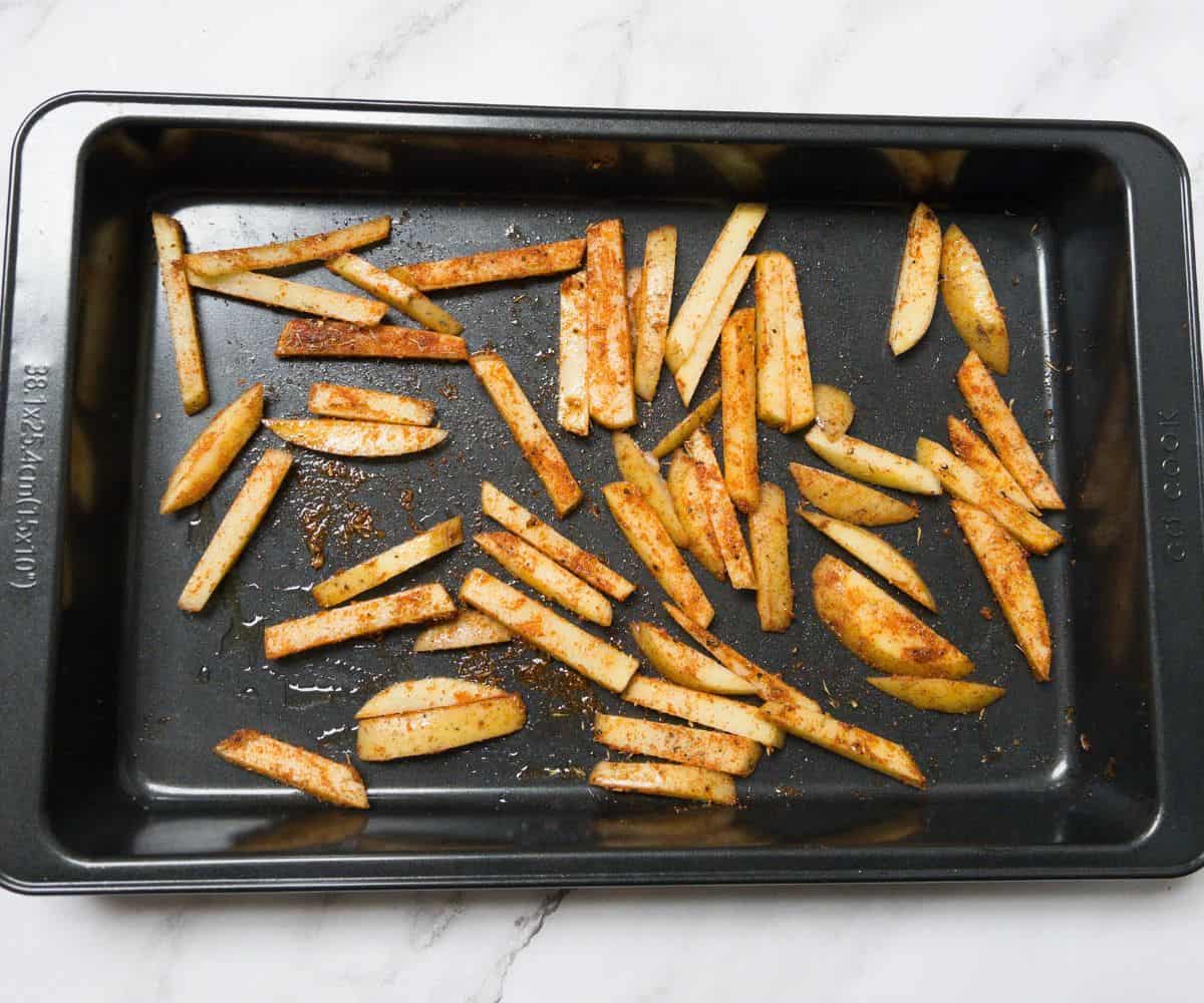 potatoes chopped into fries and coated in cajun seasoning in a roasting tray.