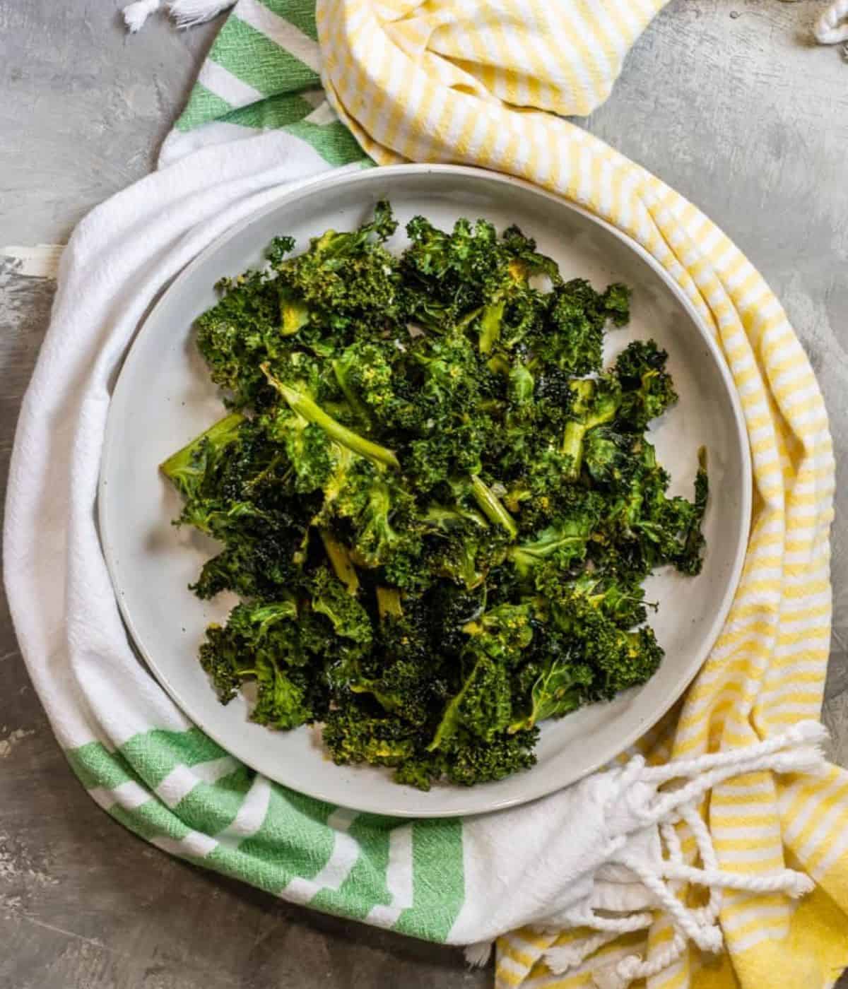 Baked kale on a white place with two tea towels placed around the outside.