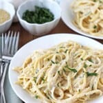 creamy linguine pasta dish in a white bowl with a bowl of green herbs in the background and a fork.