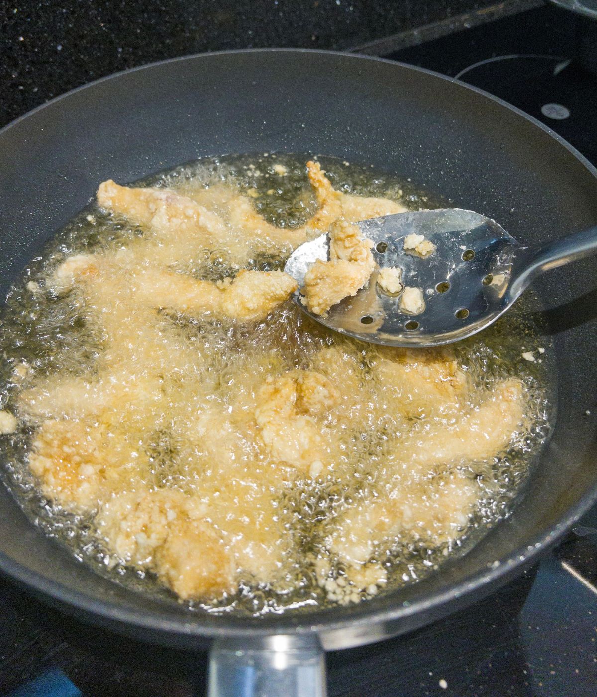 Chicken coated in flour and egg frying in the frying pan.