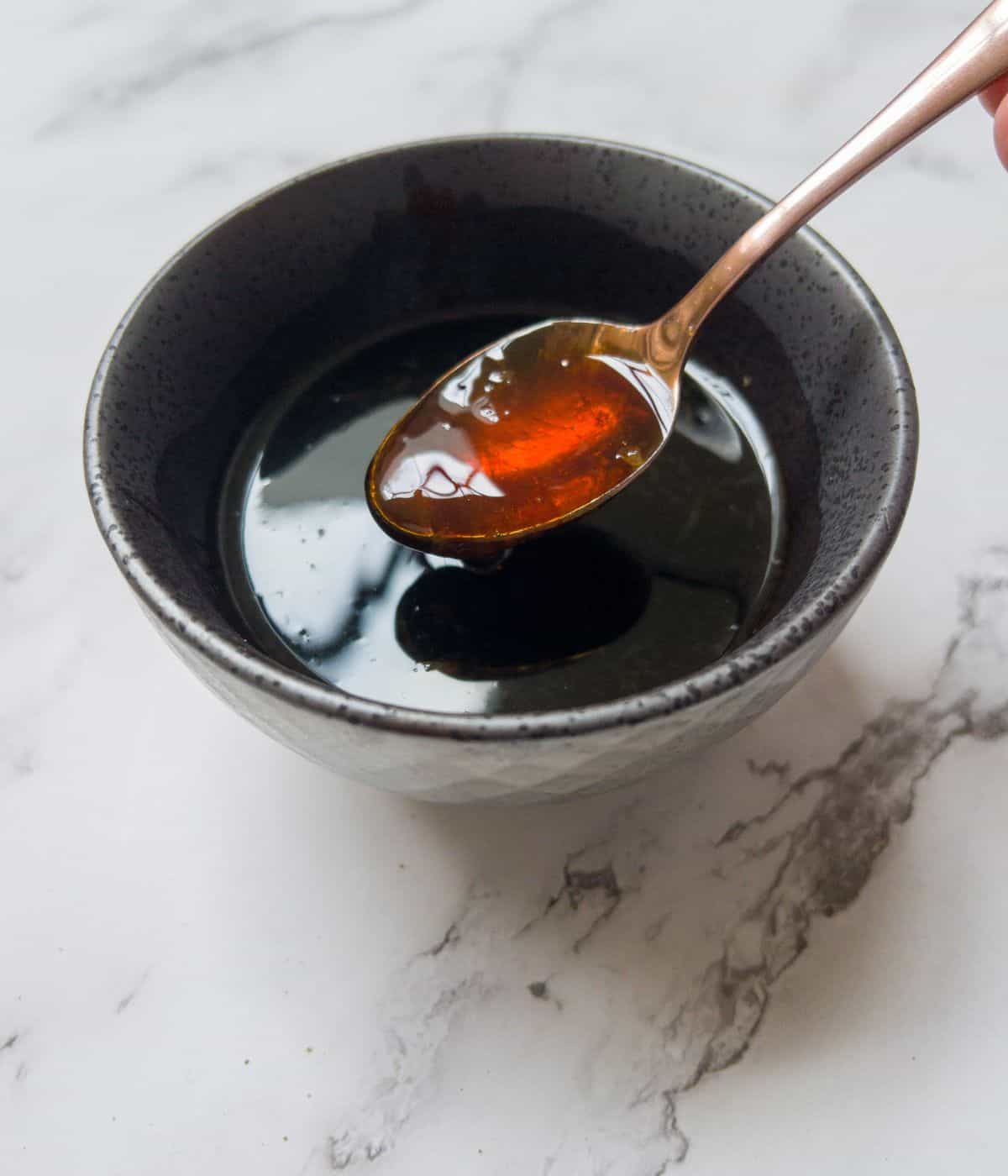A grey bowl of chinese stir fry sauce with a spoon in it.