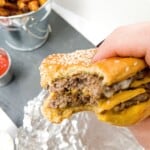 close up shot of someone holding a burger with a bite out of it with chips in the background.