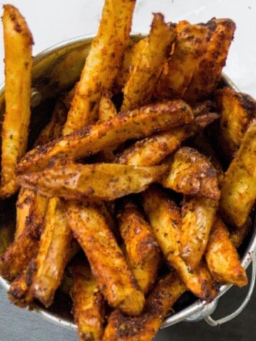 Close up of cajun fries in a small metal bucket.