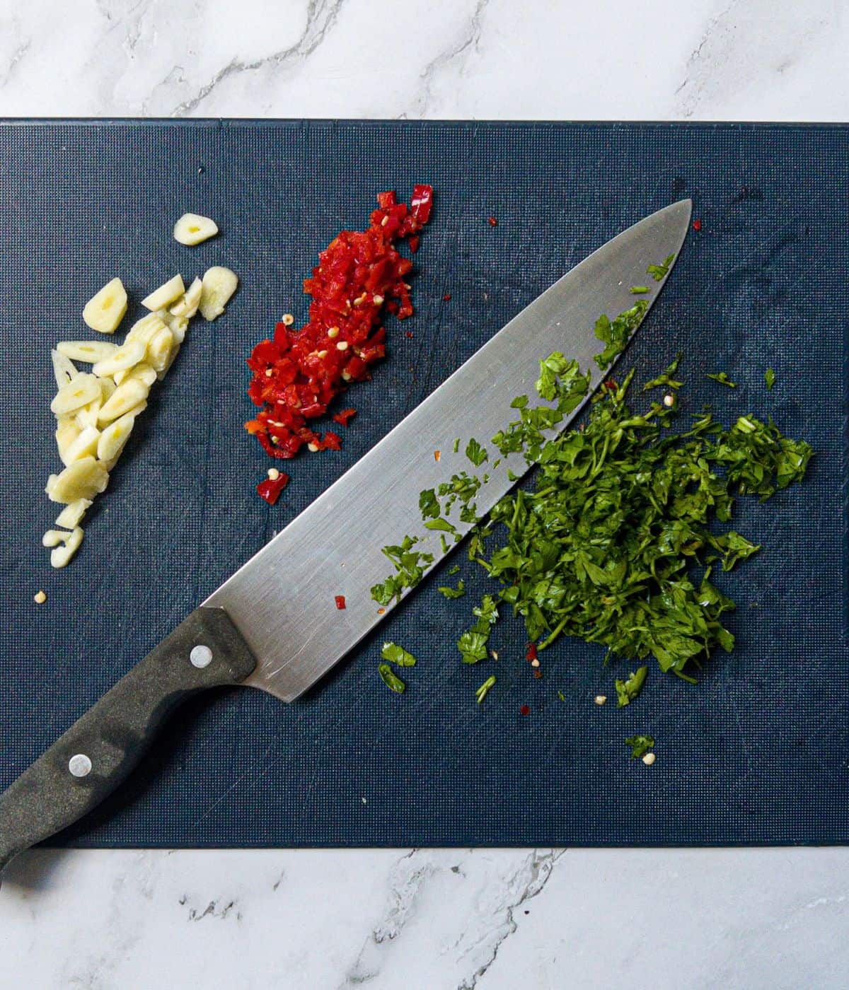 Chopped garlic, chilli and parsley on a chopping board with a knife.