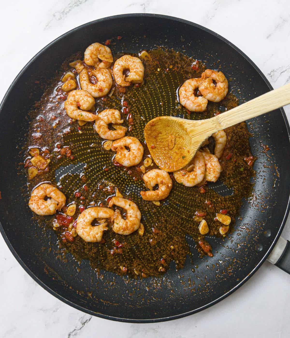 prawns with chilli and garlic being stirred in a frying pan.