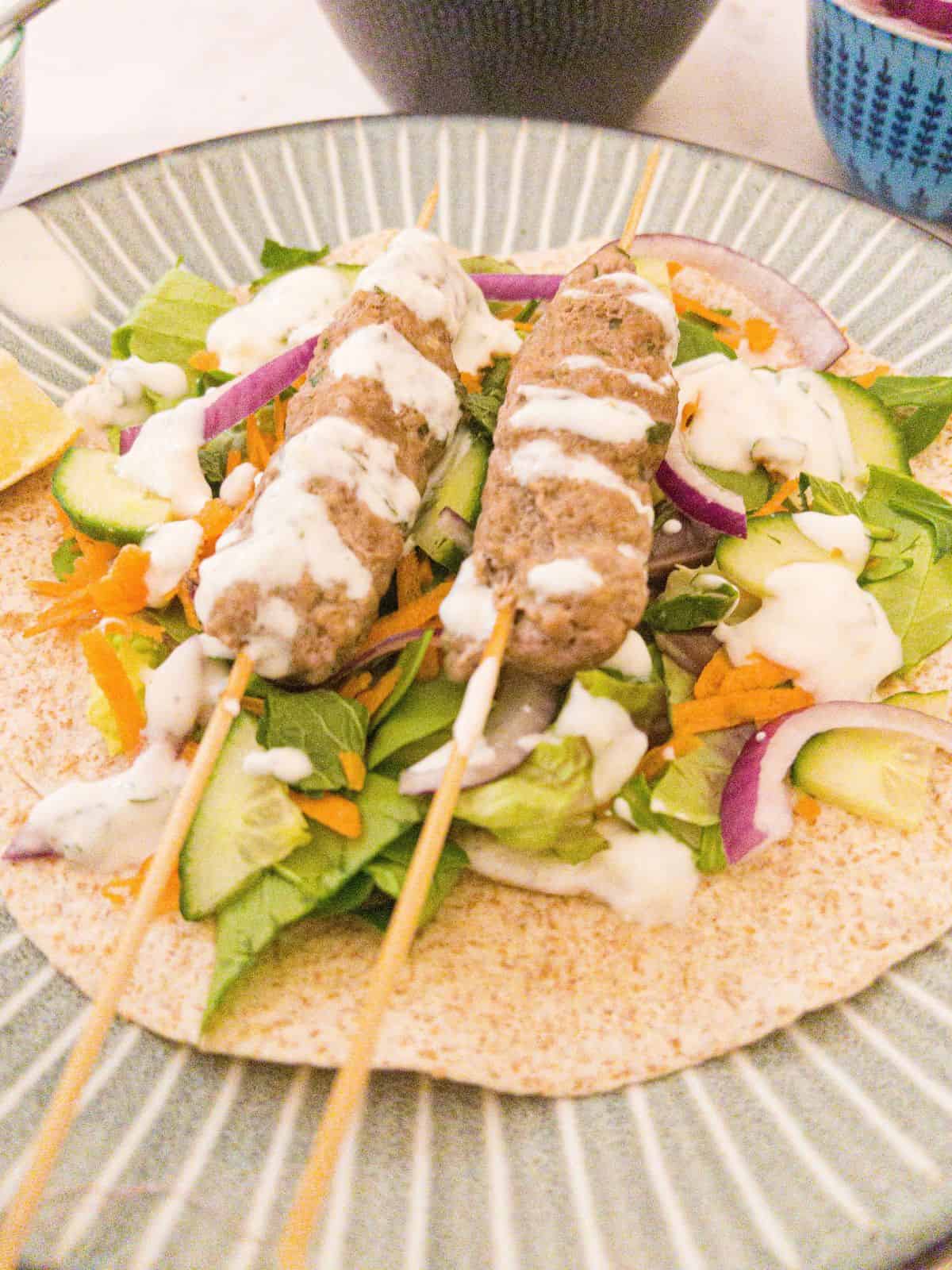 Lamb kofta kebab and salad on a blue stripy plate.