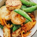 crisps tofu in a bowl with sugar snap peas.