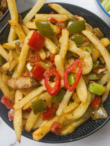 Close up of chips garnished with red and green pepper, onion, spices and red chilli.