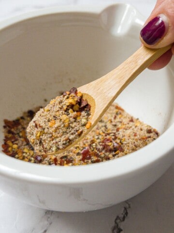 a white bowl containing salt and pepper spice seasoning, with a small wooden teaspoon in it.