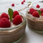 close up of two pots of tofu chocolate. mousse topped with raspberries and mint.