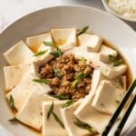 Ground pork in a white bowl with slices of silken tofu around the edge with some chopsticks lying on the side of the bowl.