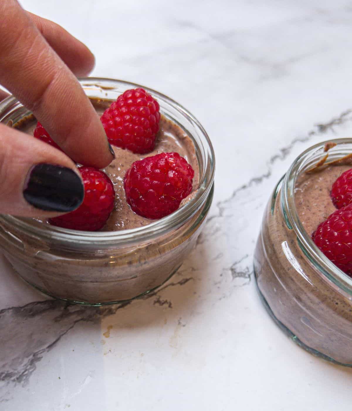 Someone putting raspberries on top of a chocolate mousse.