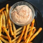 Bowl of vegan chipotle mayo on a black plate full of french fries.