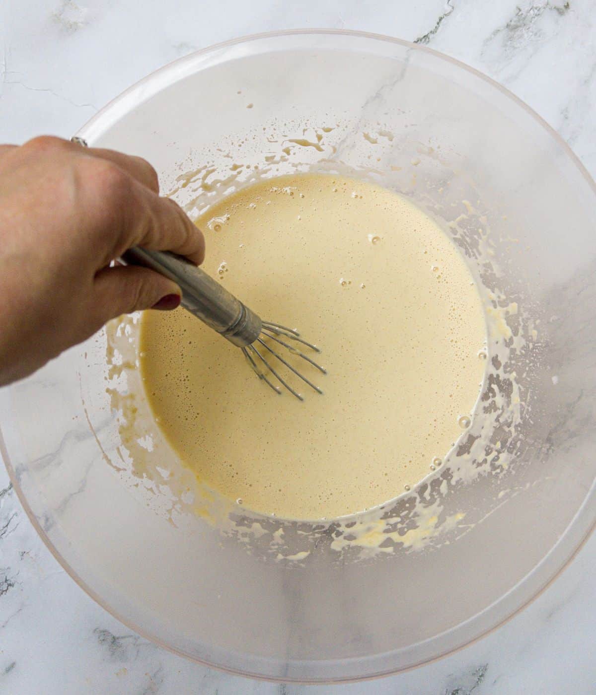 Batter mix for a crepe being whisked in a mixing bowl.