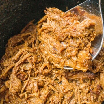 shredded bbq beef brisket in a black pot with a spoon picking up a spoonful.