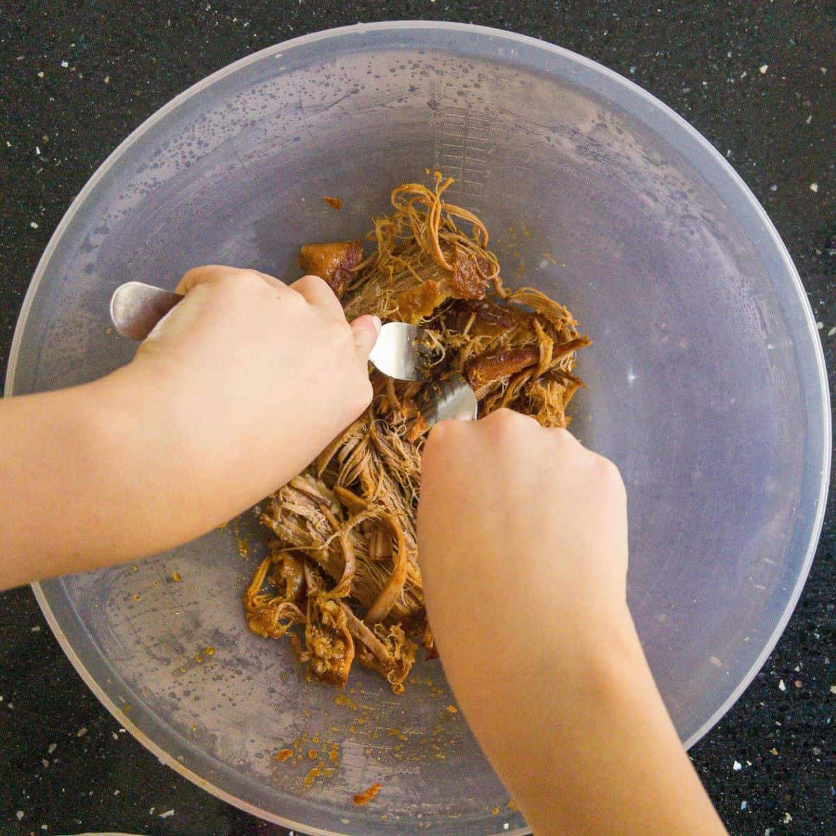 Beef being shredded in a mixing bowl with two forks.