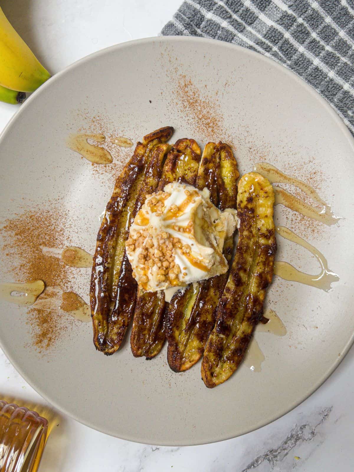 Ice cream with sprinkles sat on top of 4 caramelized bananas on a neutral plate.