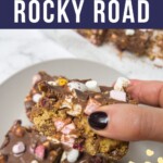 A piece of rocky road being picked up from a plate with a couple of slices on the plate too.