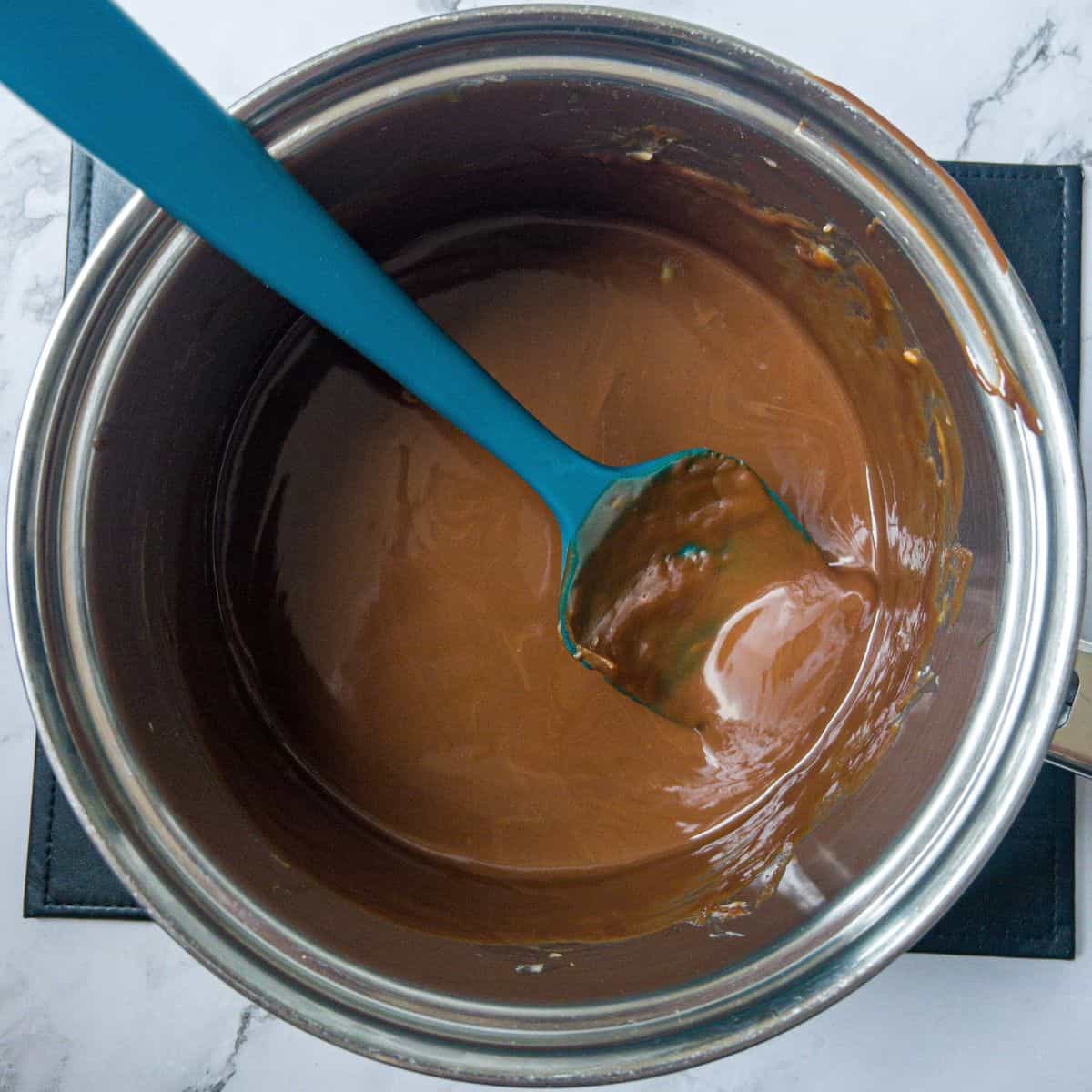 nChocolate melting in a saucepan with a blue spatula in the saucepan.