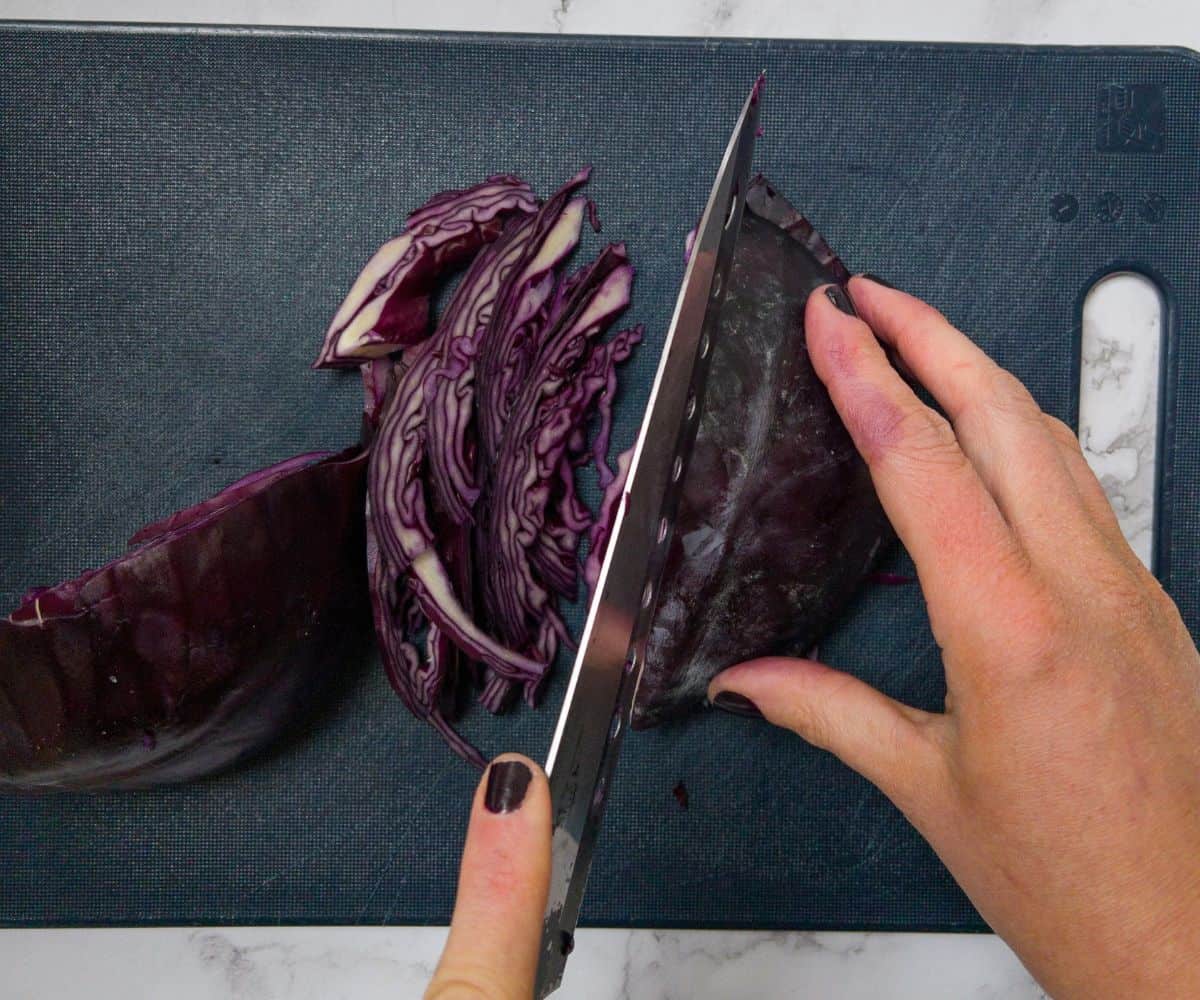 Red cabbage being sliced on a blue chopping board.
