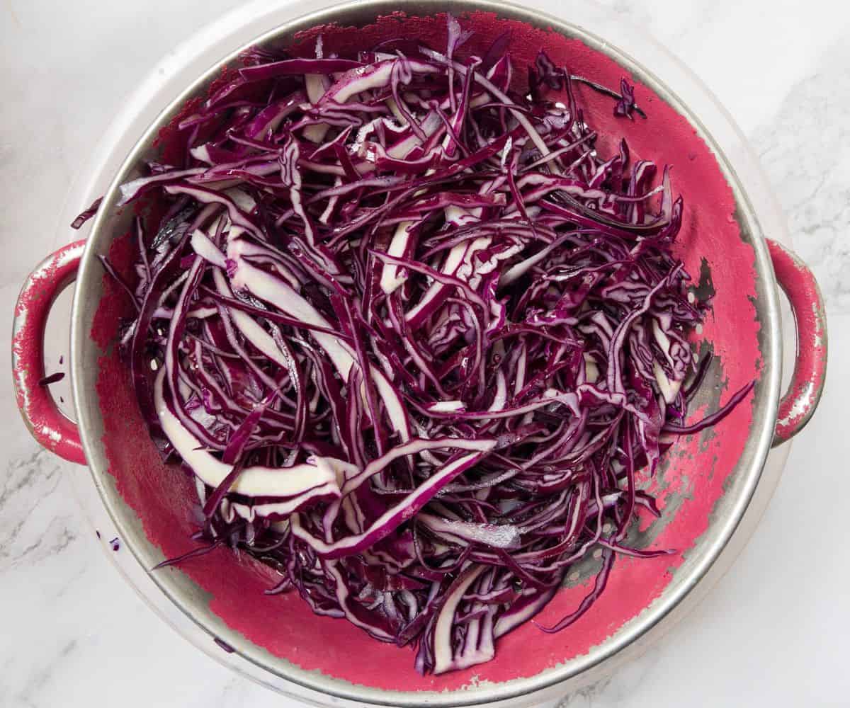 Shredded red cabbage in a red colander.